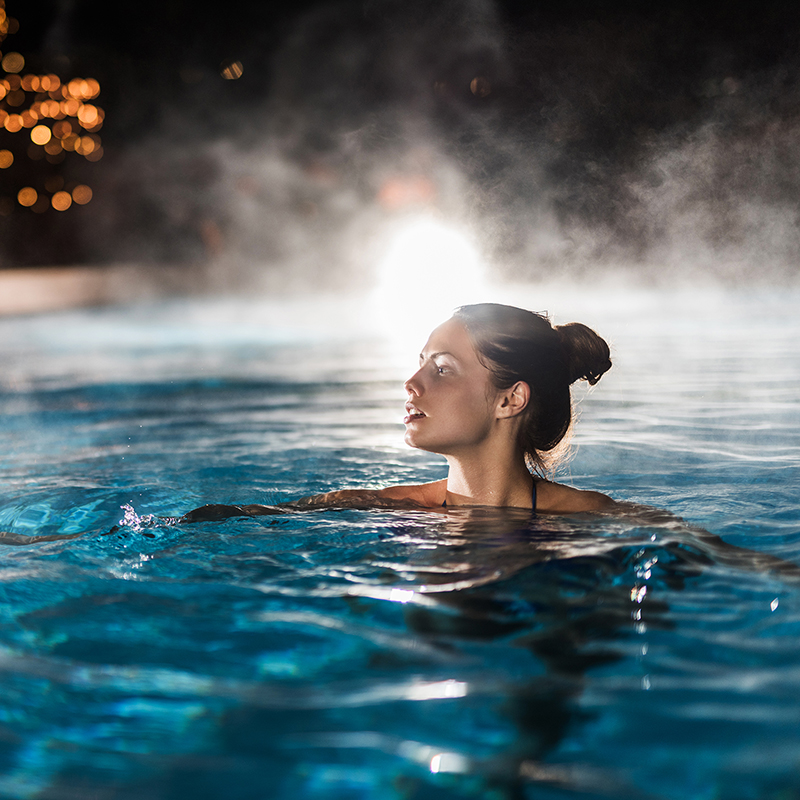 Young woman enjoying in a heated swimming pool at night.